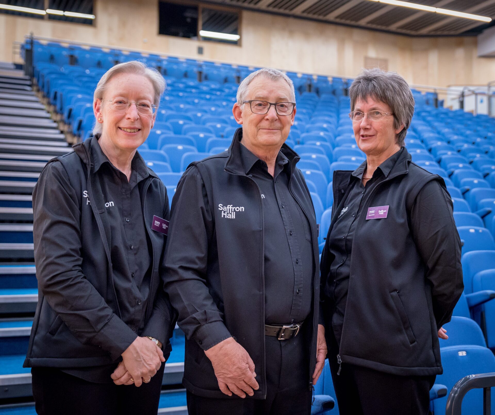 Three smiling volunteers in their stewarding uniforms