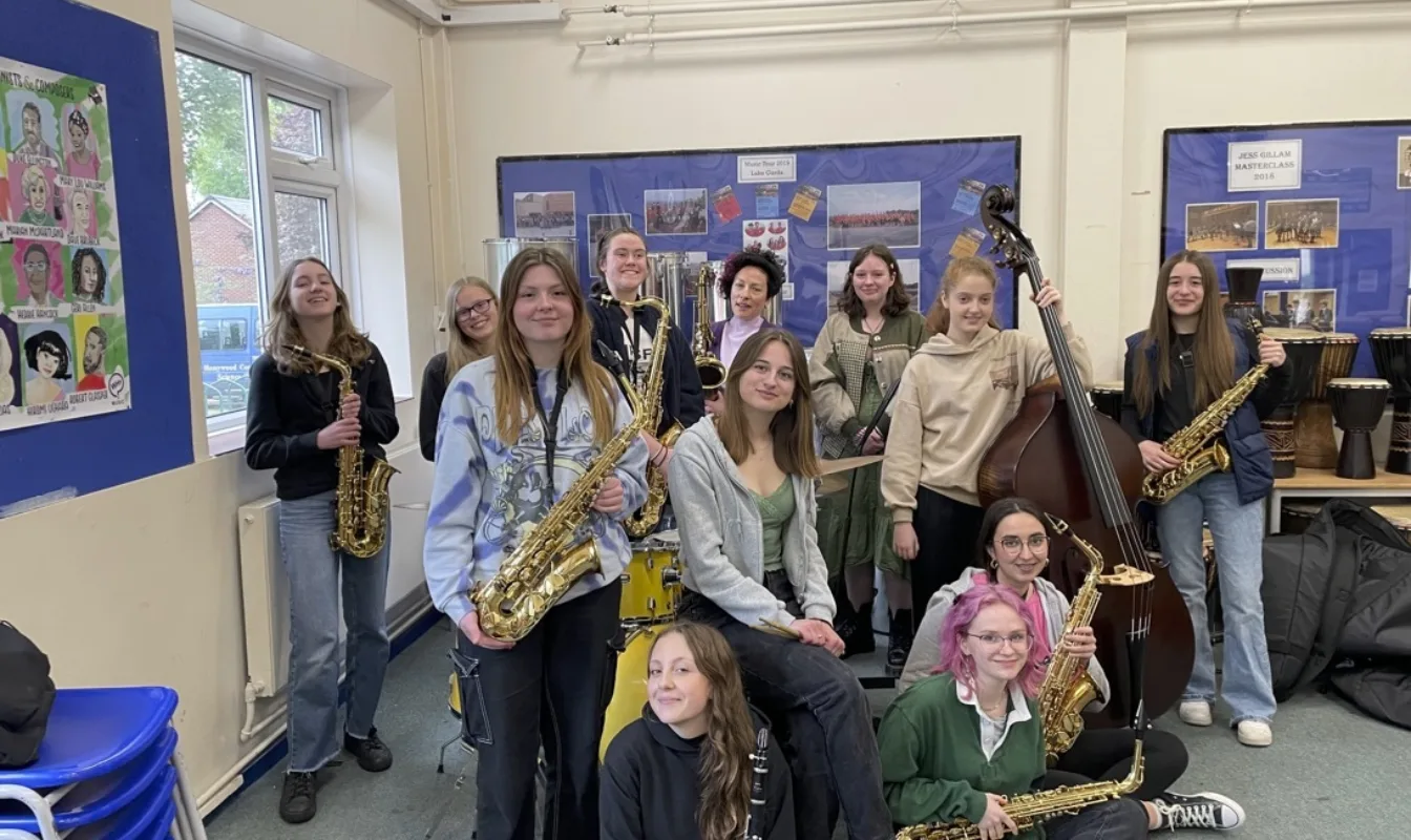 Group of young women and non-binary musicians hold their instruments in a school classroom